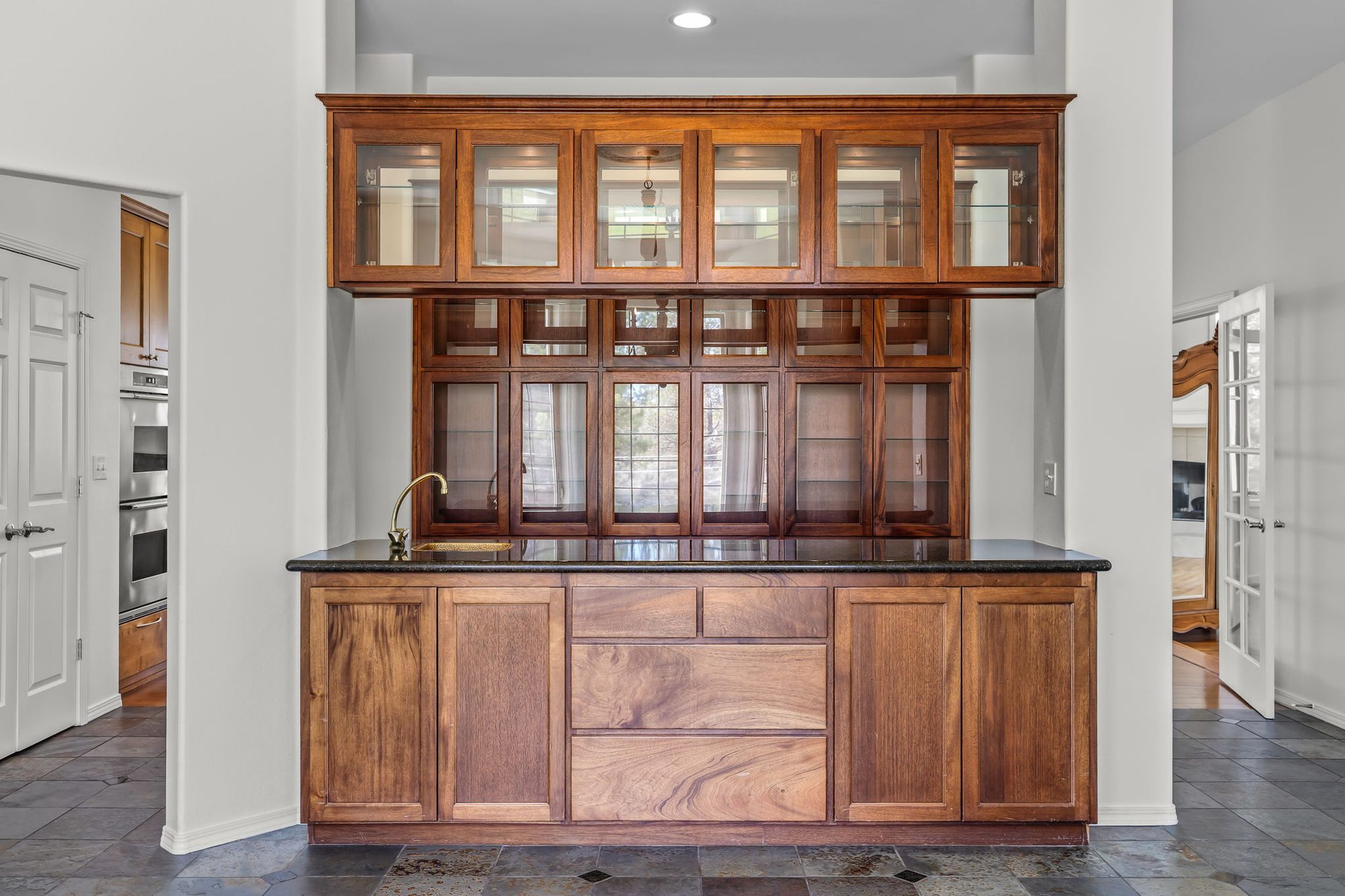 Built-in butler's bar with glass display cabinetry and granite counter