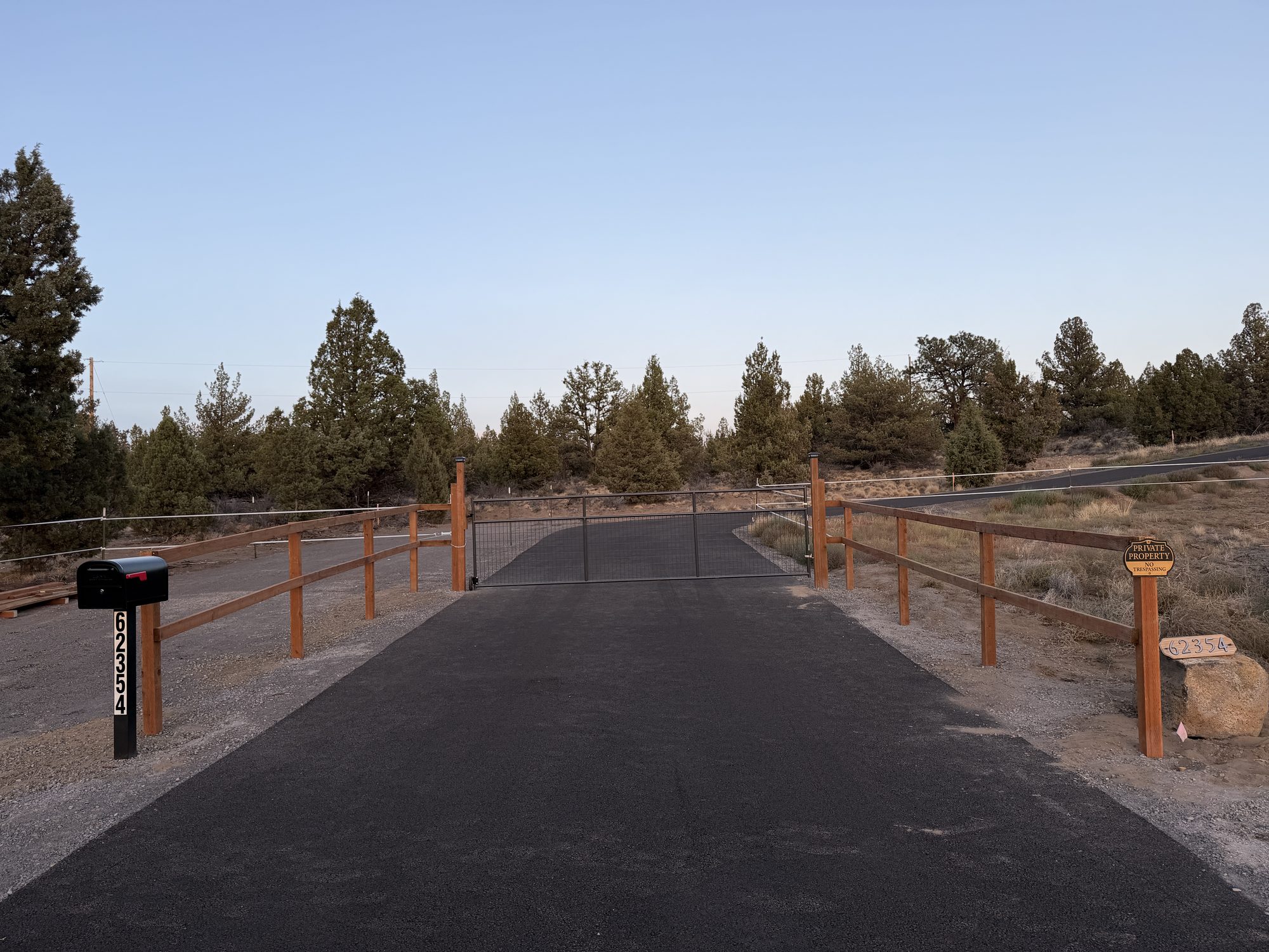 Gated private entrance with wood rail fencing and paved driveway at dusk
