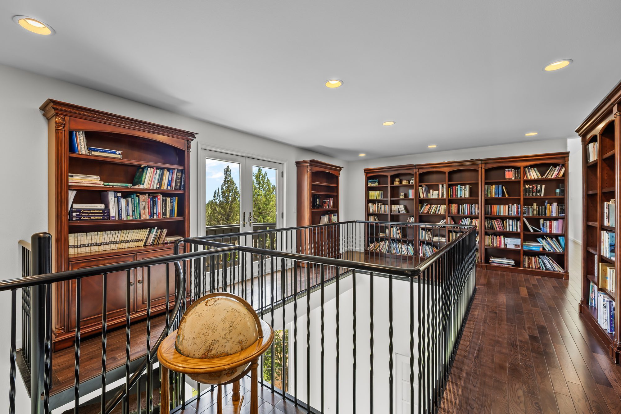 Upper-level library loft with floor-to-ceiling bookshelves and view of the pines